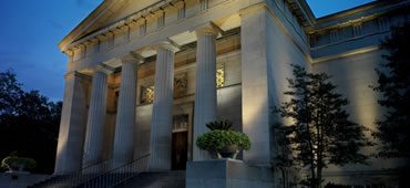 A building with columns and plants in front of it.
