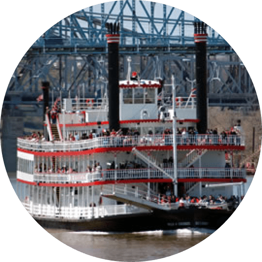 A large paddle boat on the water near a bridge.